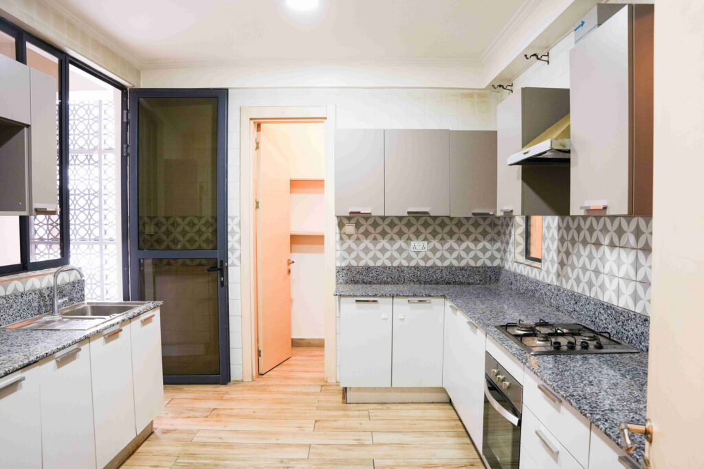 L-shaped fitted kitchen with white cabinets, granite worktops and decorative tile splashback at 5th Park Heights