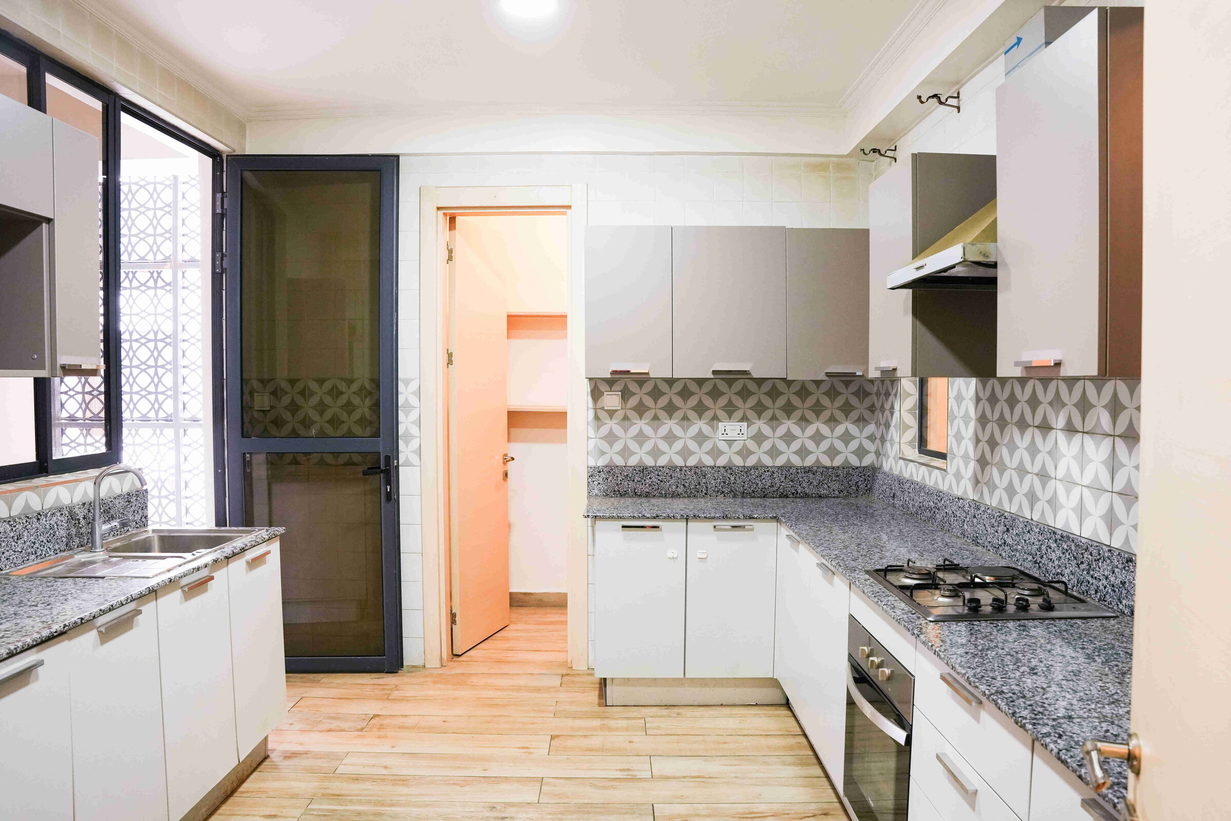 L-shaped fitted kitchen with white cabinets, granite worktops and decorative tile splashback at 5th Park Heights